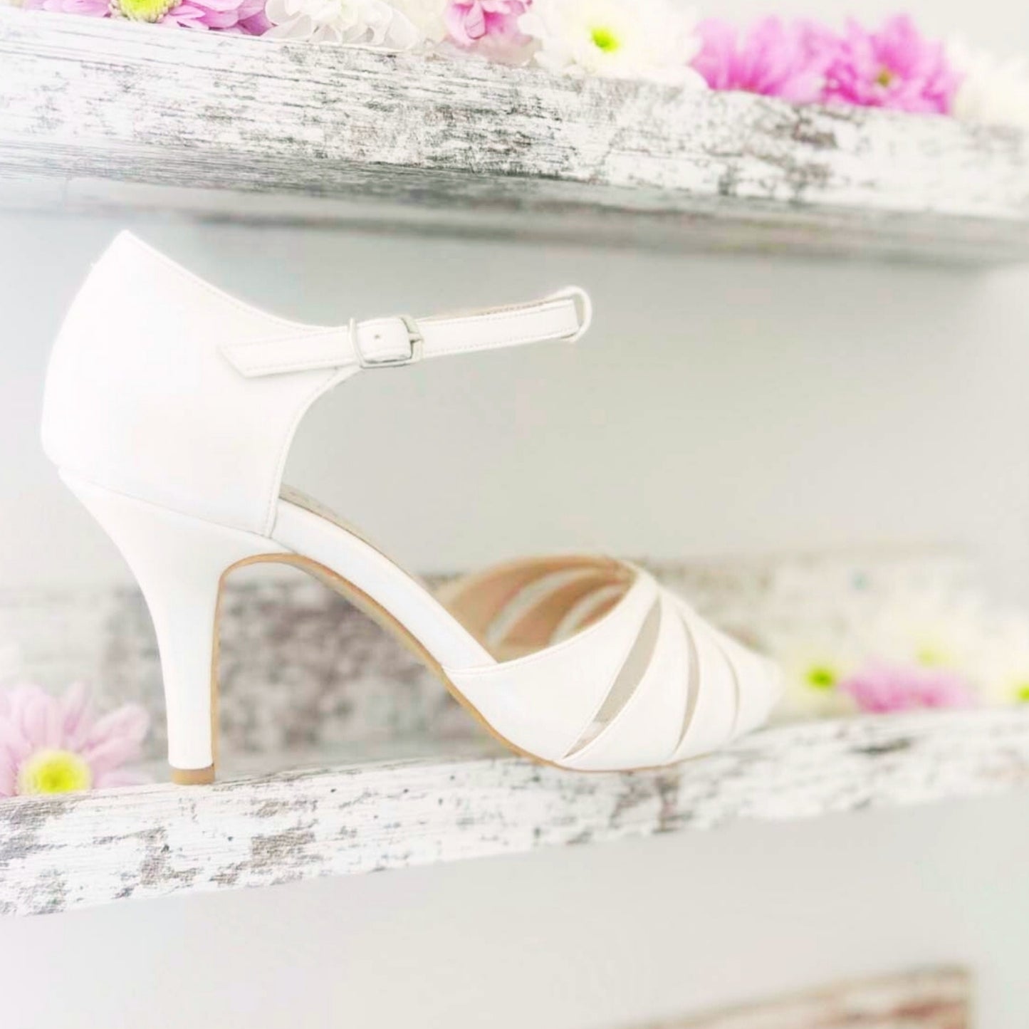 An ivory wedding shoe rests on a shelf adorned with delicate flowers, creating an elegant display.
