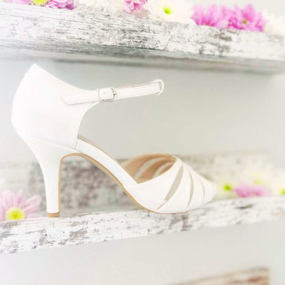 An ivory wedding shoe rests on a shelf adorned with delicate flowers, creating an elegant display.