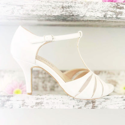 Elegant ivory wedding shoes resting on a shelf surrounded by vibrant flowers.