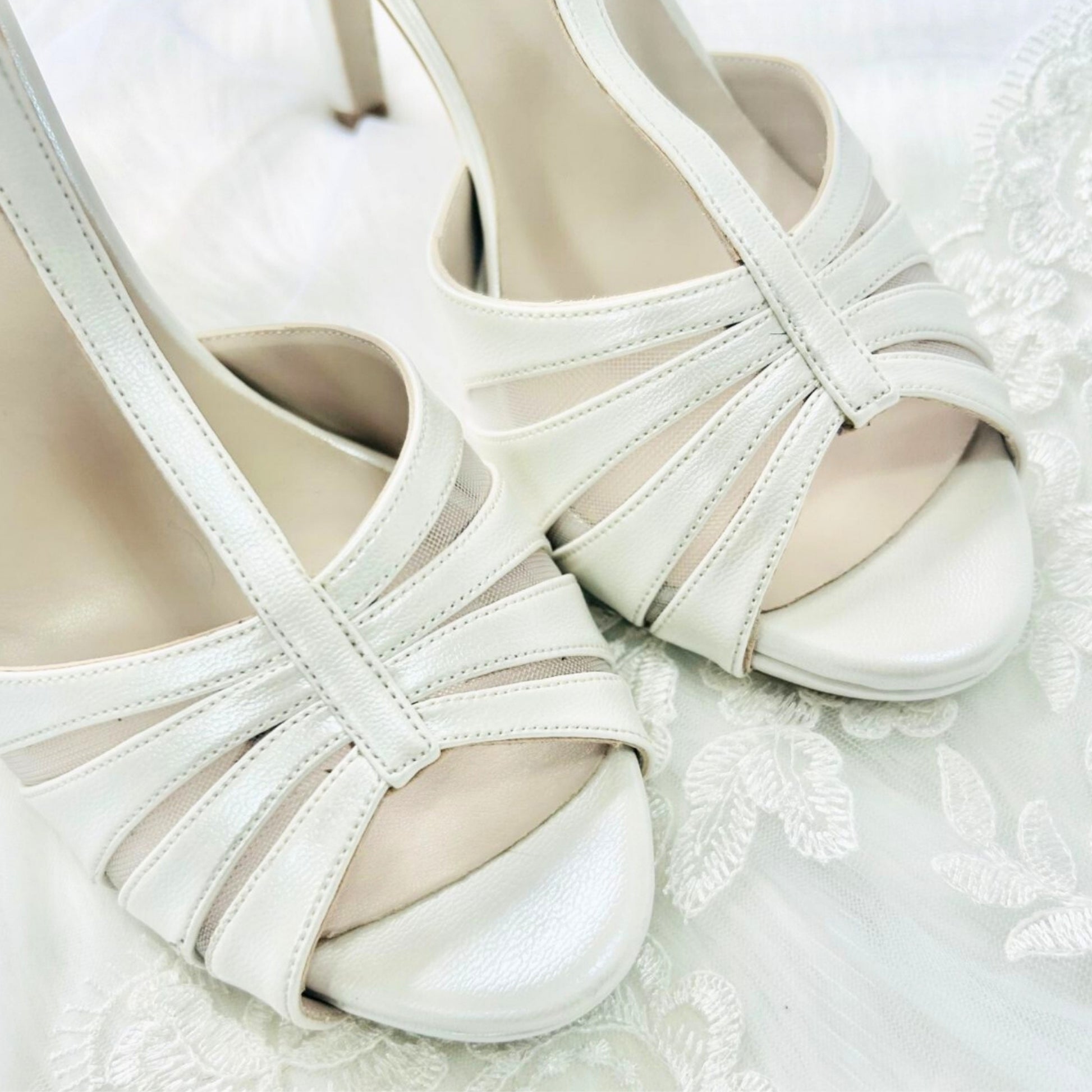 A pair of elegant ivory wedding shoes resting on a delicate lace background, showcasing their intricate design.